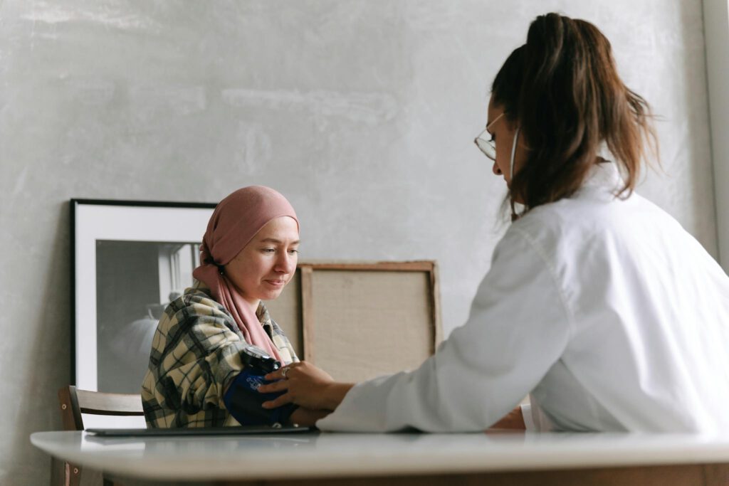 Doctor checks blood pressure of a patient wearing a headscarf indoors, focused on healthcare.